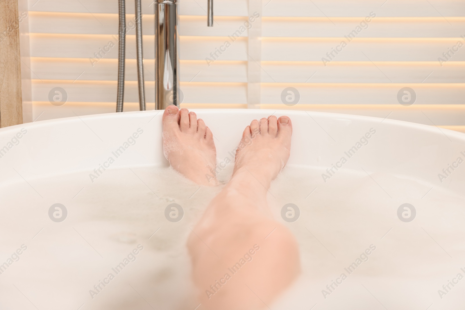 Photo of Woman taking bath with foam in tub indoors, closeup