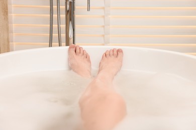 Woman taking bath with foam in tub indoors, closeup