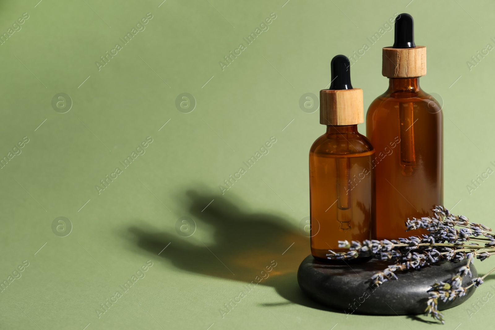 Photo of Composition with bottles of face serum, spa stone and beautiful flowers on light green background. Space for text