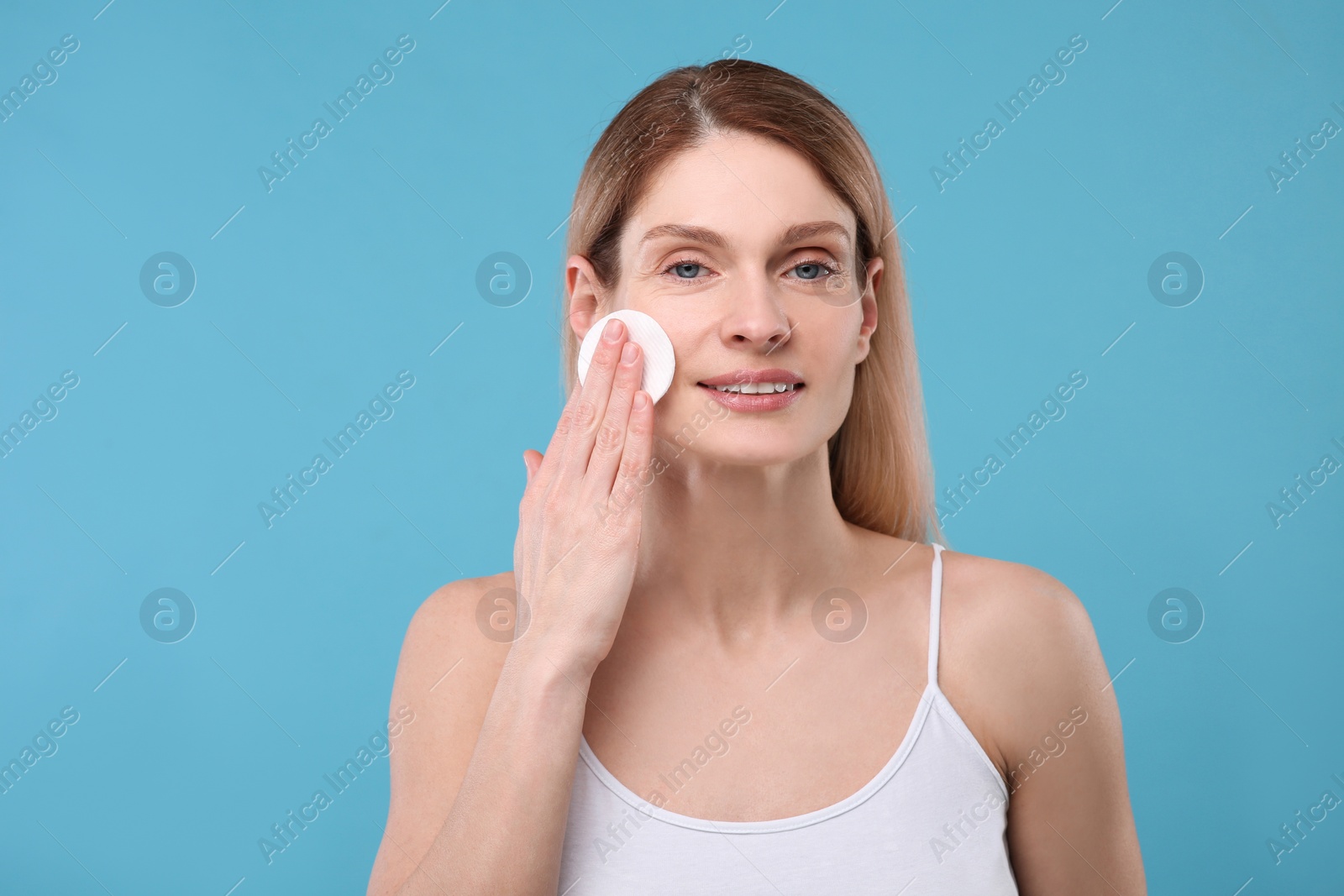 Photo of Beautiful woman removing makeup with cotton pad on light blue background, space for text