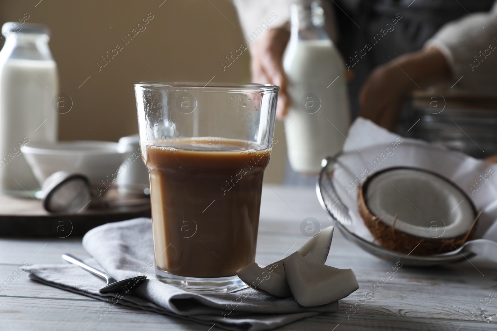 Photo of Glass of coffee with coconut milk and nuts on white wooden table, selective focus. Space for text