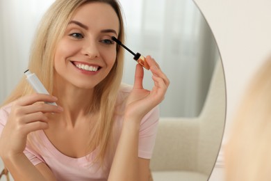 Photo of Beautiful woman applying mascara near mirror at home