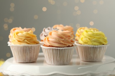 Tasty cupcakes on white stand against blurred lights, closeup
