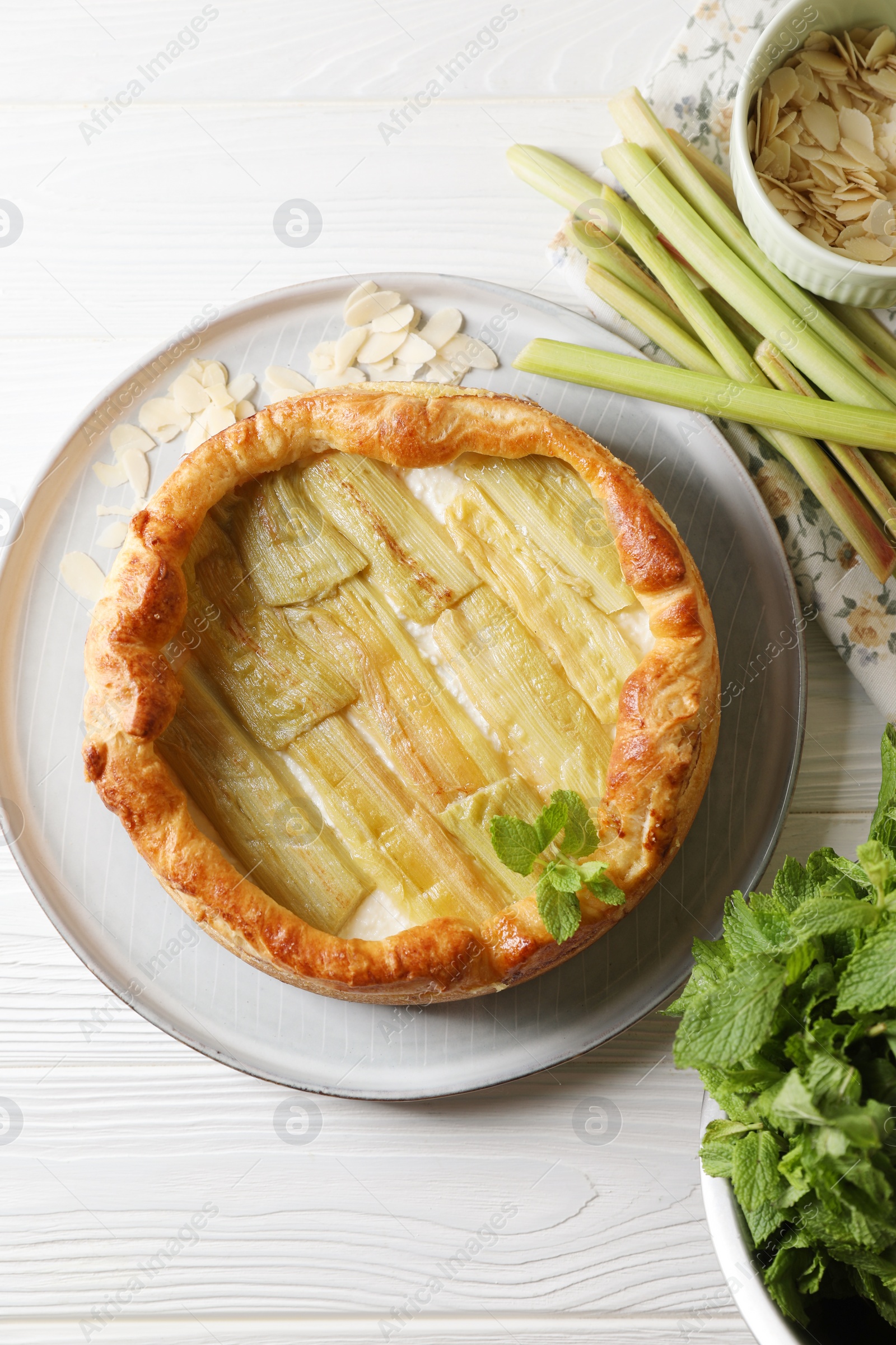 Photo of Freshly baked rhubarb pie and stalks on white wooden table, flat lay