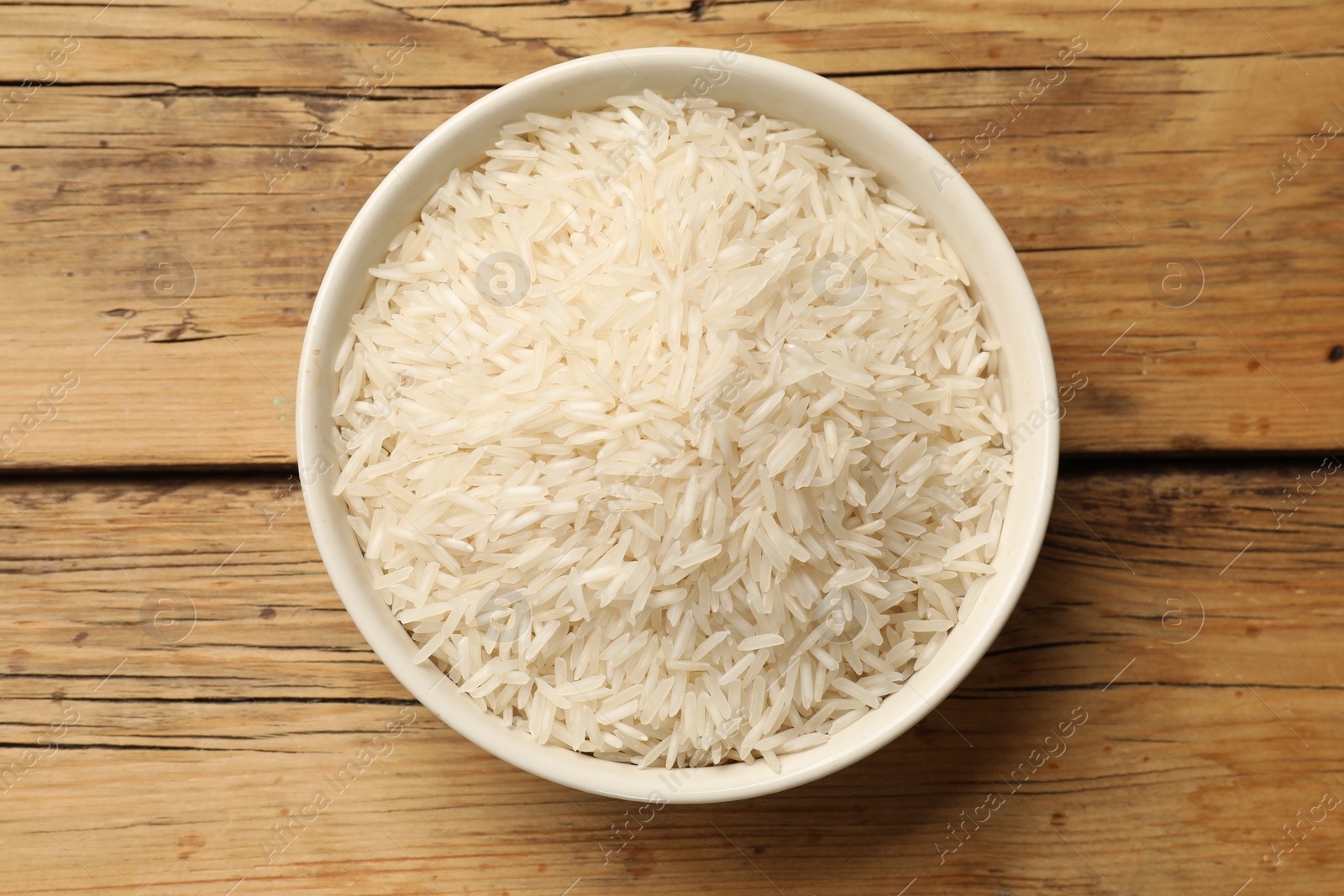 Photo of Raw basmati rice in bowl on wooden table, top view