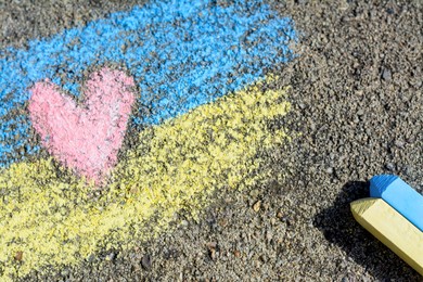 Photo of National flag of Ukraine with heart drawn by color chalk and sticks on asphalt, closeup