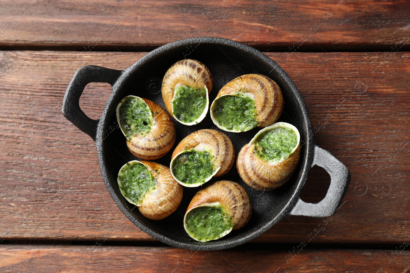 Photo of Delicious cooked snails in baking dish on wooden table, top view