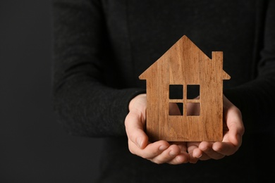 Woman holding wooden house on dark background, closeup. Home insurance