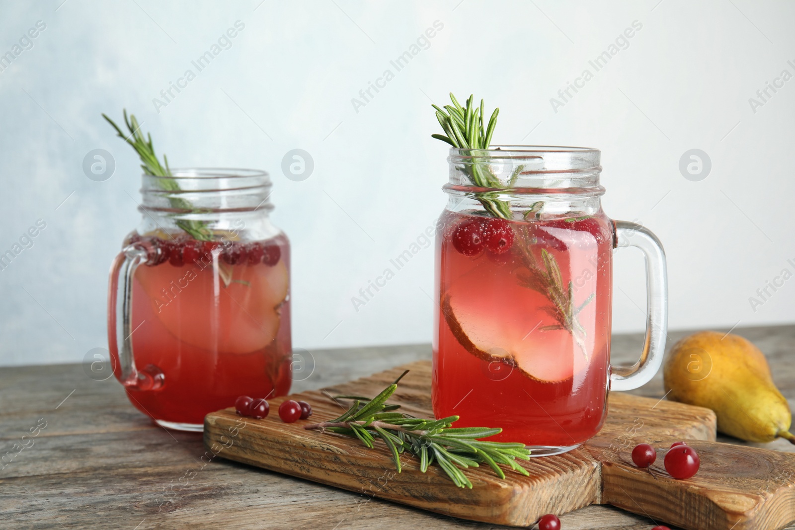 Photo of Tasty refreshing cranberry cocktail with rosemary in mason jars on table