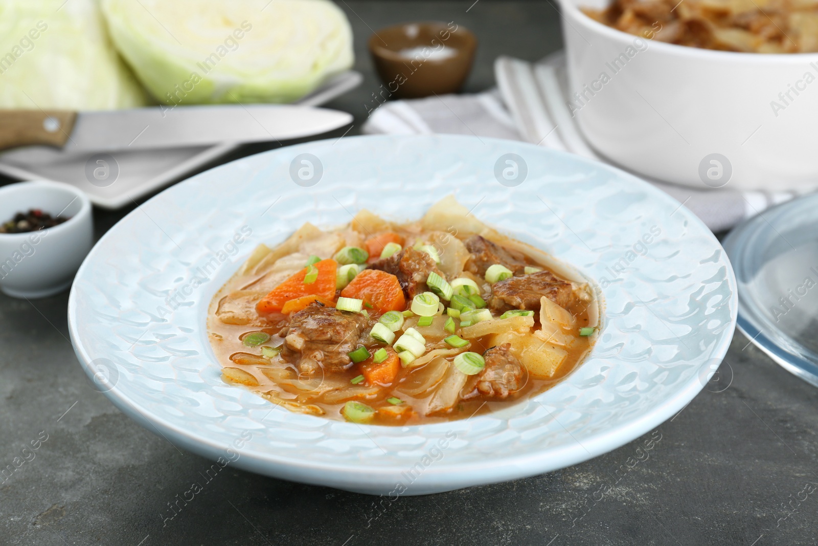 Photo of Tasty cabbage soup with meat, green onion and carrot on grey table, closeup