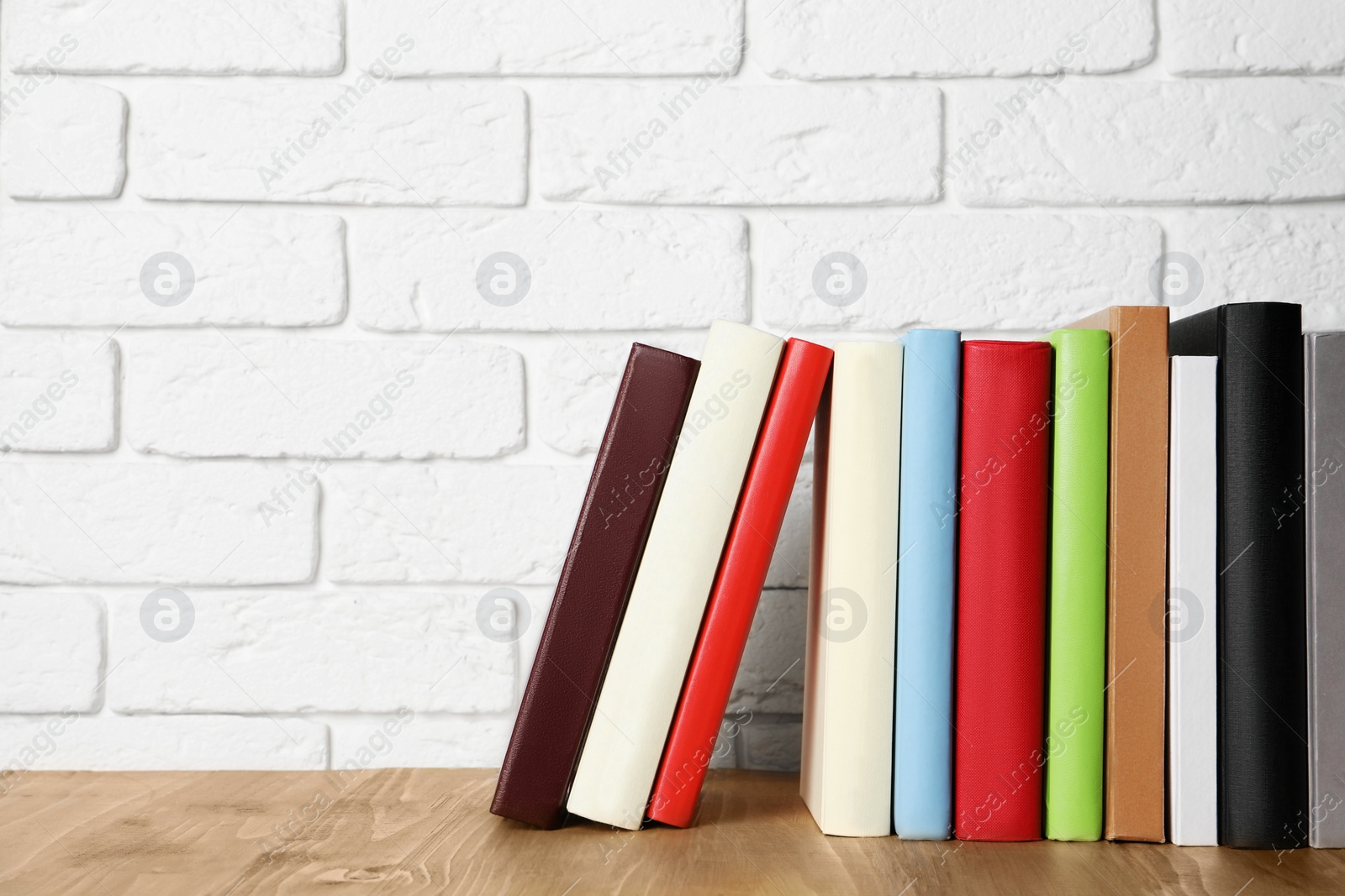 Photo of Books on wooden table near white brick wall, space for text