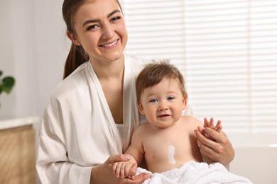 Photo of Happy mother holding her baby with body cream on skin at home