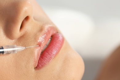 Photo of Young woman getting lips injection on blurred background, space for text. Cosmetic surgery