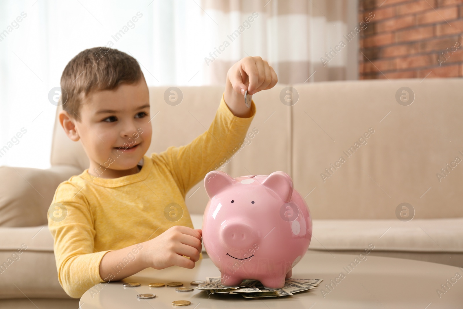 Photo of Little boy with piggy bank and money at home