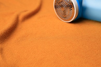 Modern fabric shaver on orange cloth with lint, closeup. Space for text