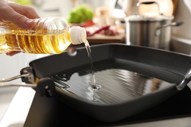 Photo of Man pouring cooking oil into frying pan in kitchen, closeup