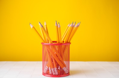 Many sharp pencils in holder on light table against yellow background