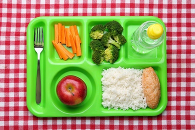 Serving tray with healthy food on checkered background, top view. School lunch