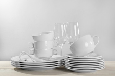 Photo of Set of clean dishware and glasses on white wooden table against light background