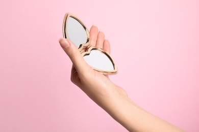 Photo of Woman holding stylish heart shaped cosmetic pocket mirror on pink background, closeup