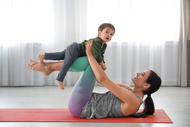 Photo of Young woman doing exercise with her son indoors. Home fitness