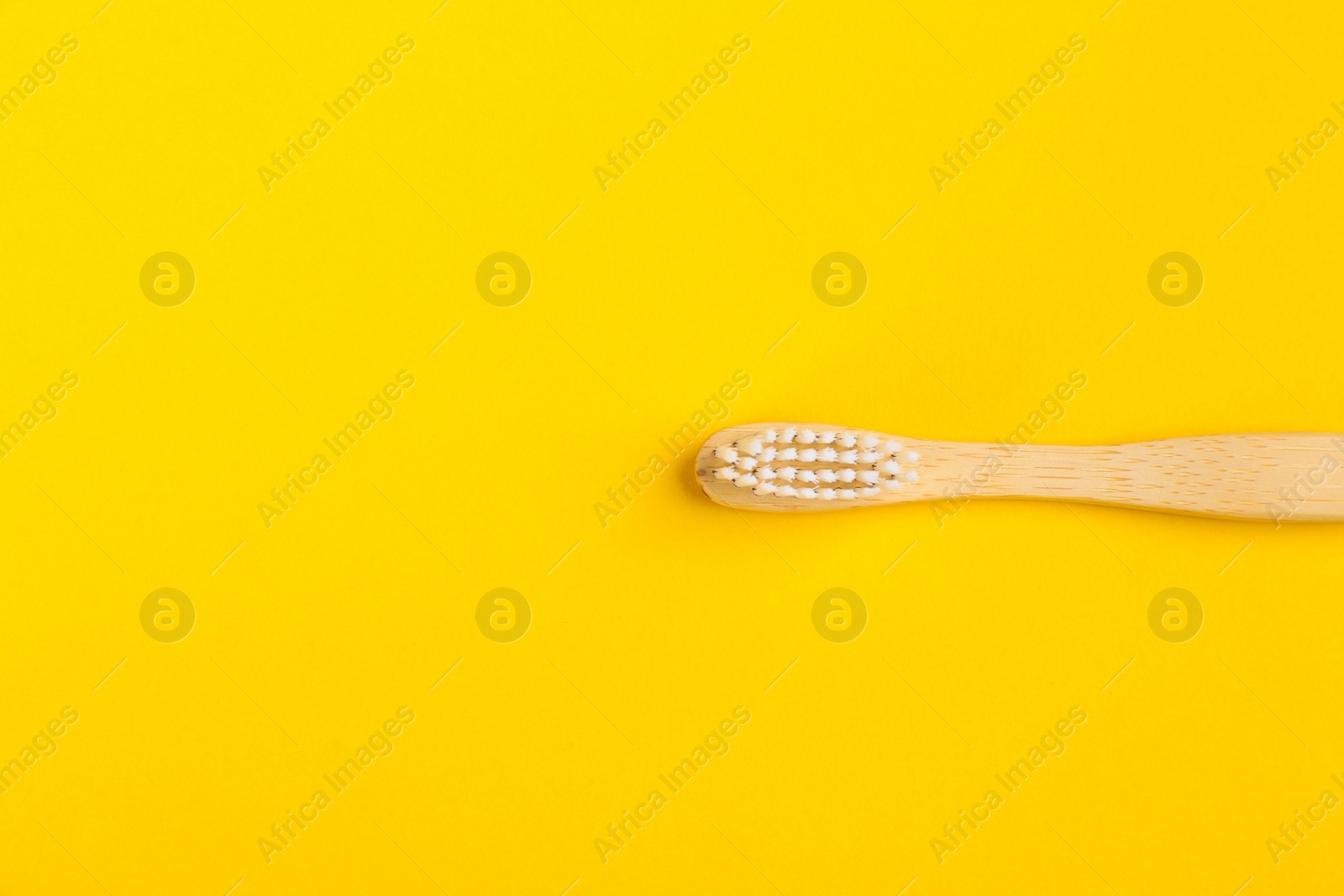 Photo of Toothbrush made of bamboo on yellow background, top view. Space for text