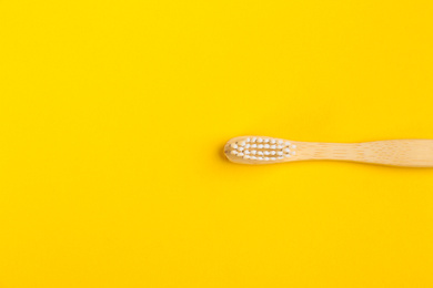 Toothbrush made of bamboo on yellow background, top view. Space for text