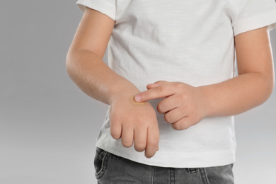 Photo of Little boy with sticking plaster on hand against light grey background, closeup