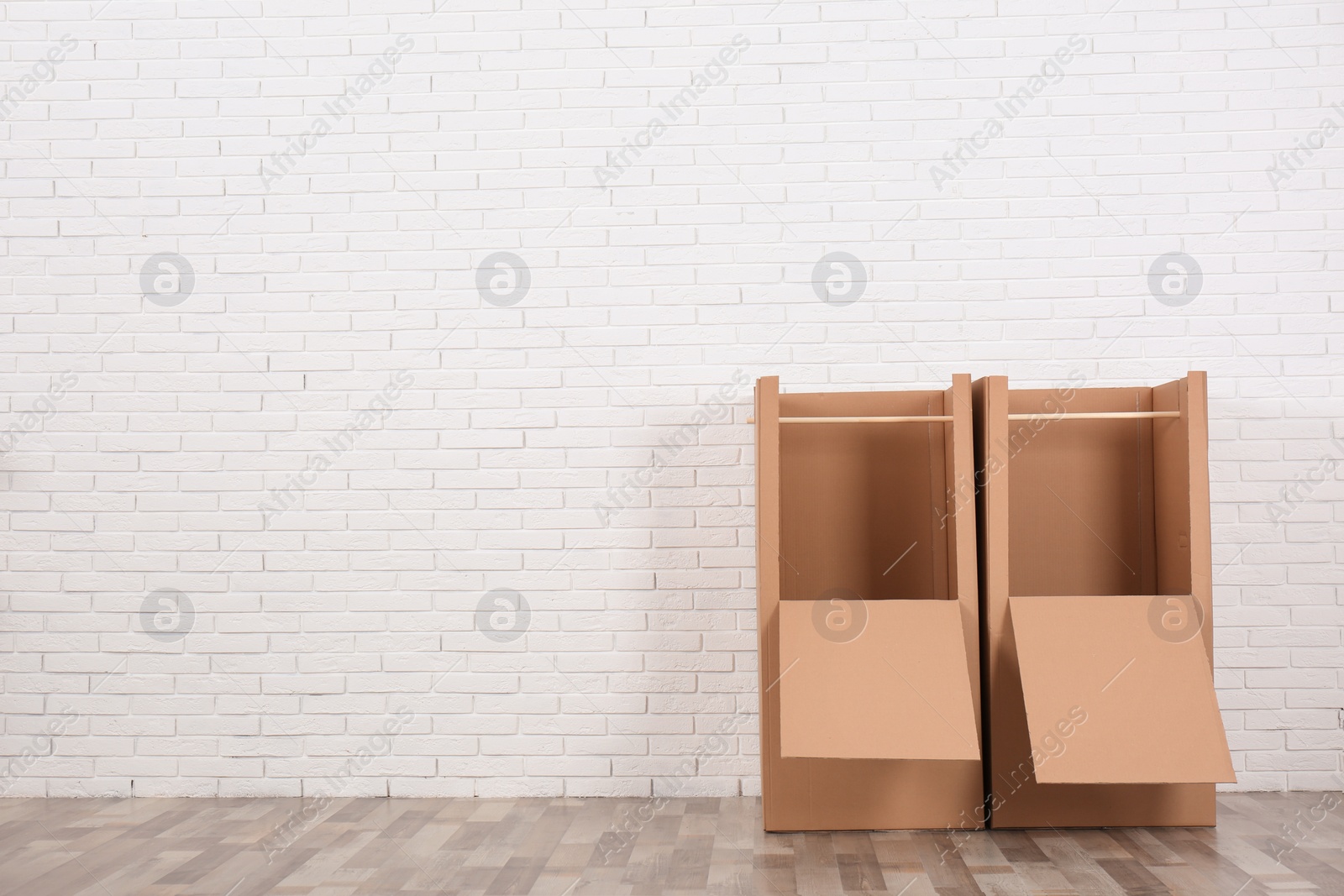 Photo of Empty cardboard wardrobe boxes against brick wall indoors. Space for text