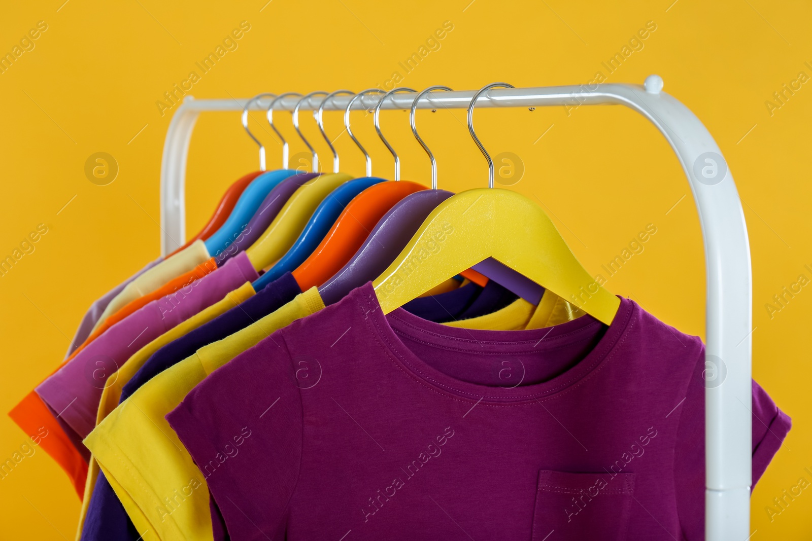 Photo of Rack with stylish children clothes on yellow background, closeup