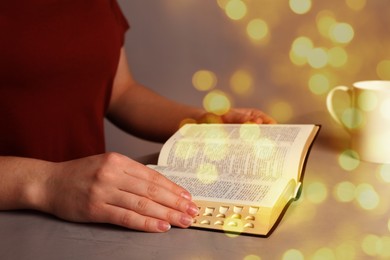 Woman reading Bible at stone table, closeup. Bokeh effect