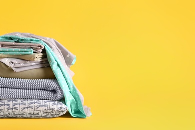 Stack of clean bed linen and pillow on yellow background. Space for text