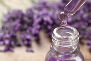 Photo of Natural oil dripping into bottle and lavender flowers on table, closeup with space for text. Cosmetic product