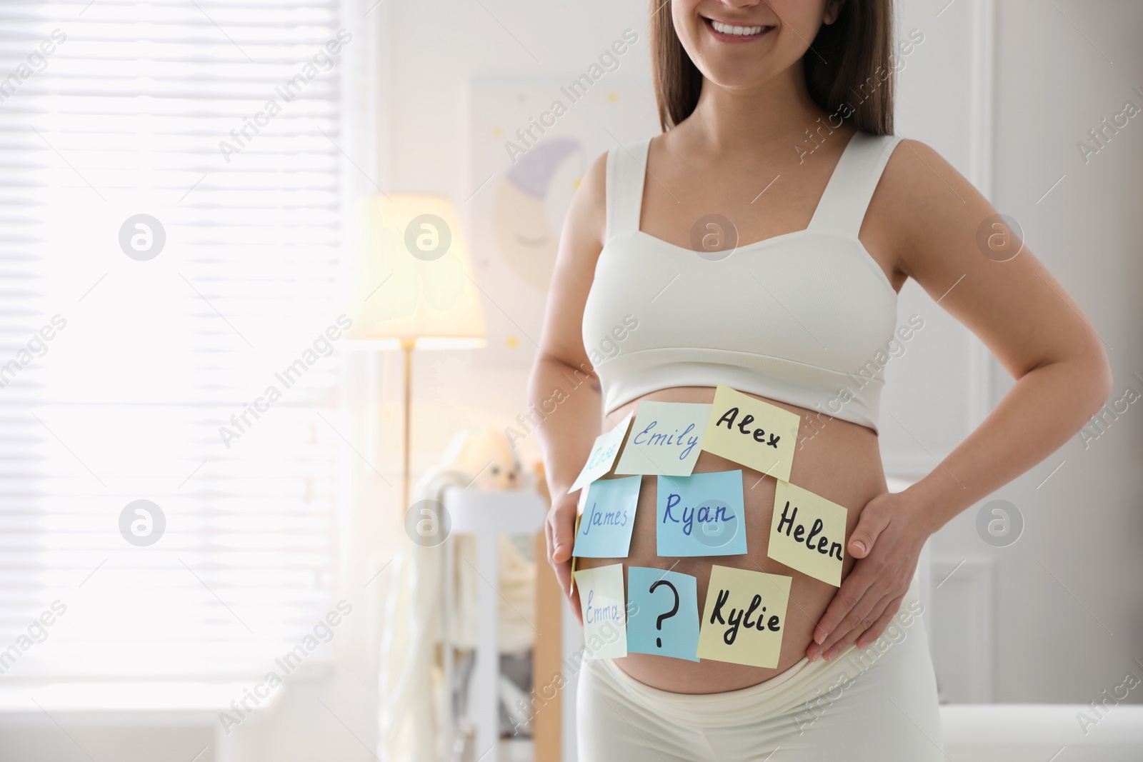 Photo of Pregnant woman with different baby names on belly at home, closeup. Space for text