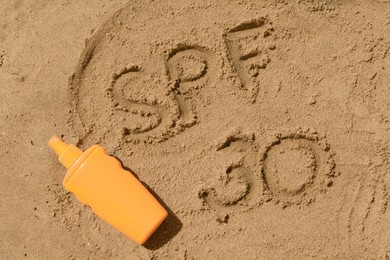 Photo of Abbreviation SPF 30 written on sand and blank bottle of sunscreen at beach, top view