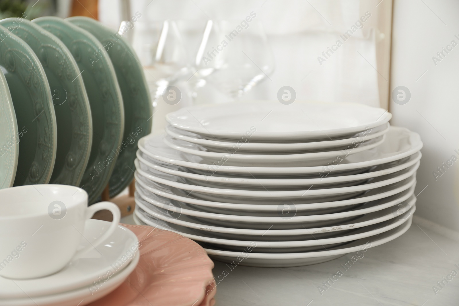 Photo of Clean plates, cup and glasses on white marble table in kitchen