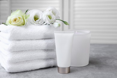 Photo of Towels, tube of lotion, scented candle and flowers on grey table indoors
