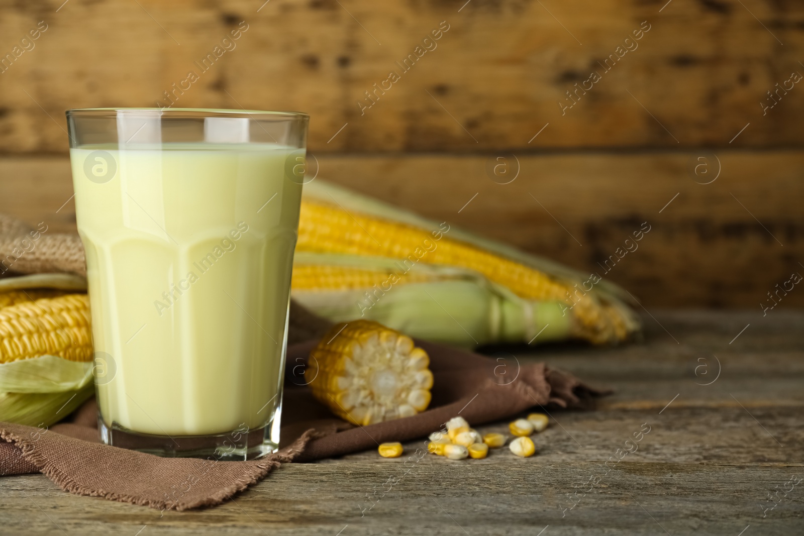 Photo of Freshly made corn milk in glass on wooden table. Space for text