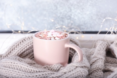 Photo of Cup of aromatic cacao with marshmallows and   warm scarf on window sill