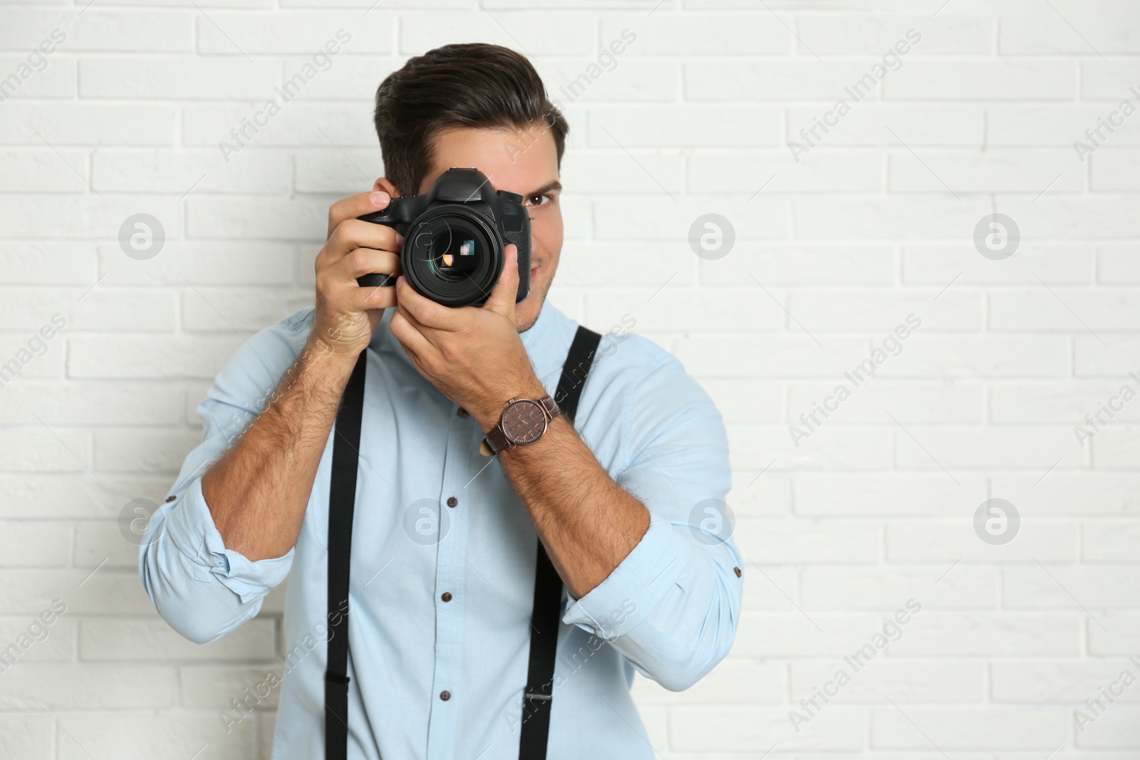 Photo of Professional photographer working near white brick wall in studio. Space for text