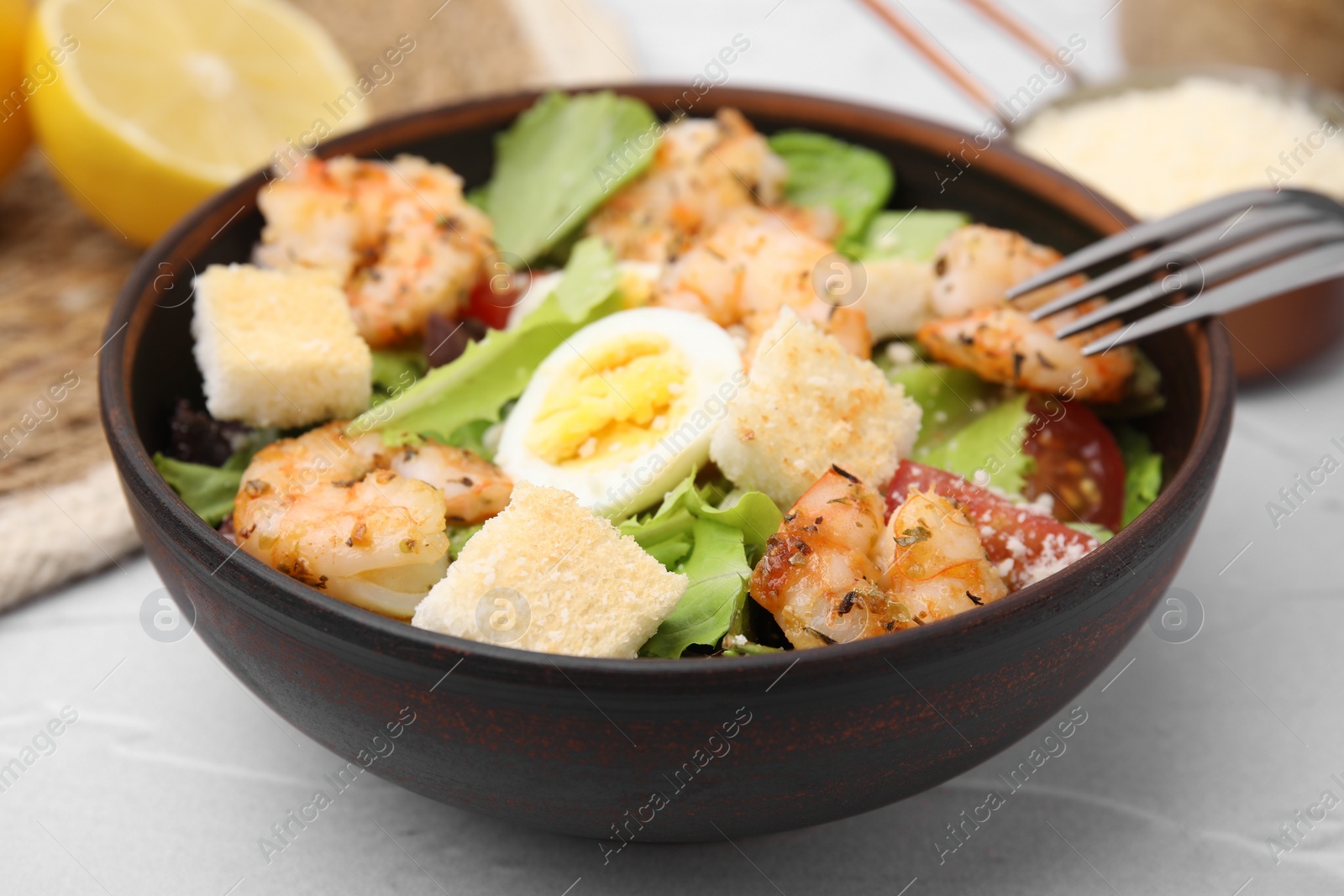 Photo of Delicious Caesar salad with shrimps and fork served on white table, closeup