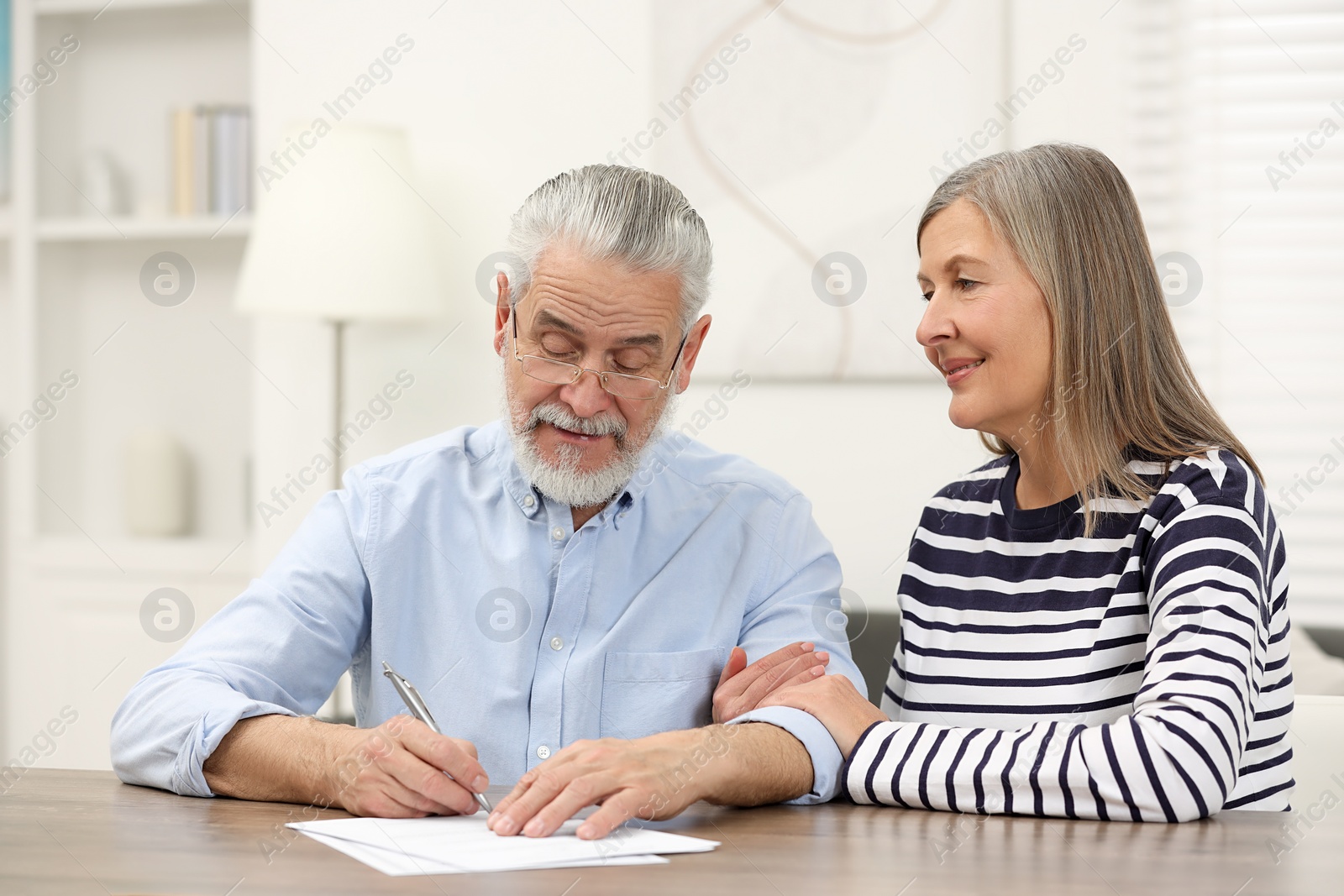 Photo of Happy senior couple signing Last Will and Testament indoors