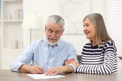 Photo of Happy senior couple signing Last Will and Testament indoors