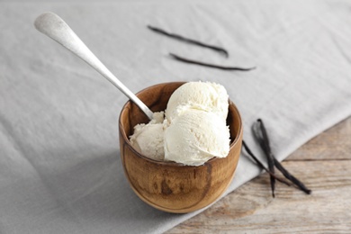 Photo of Wooden bowl with tasty vanilla ice cream on table