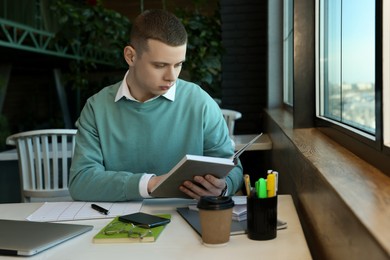 Photo of Young male student with books studying at table in cafe