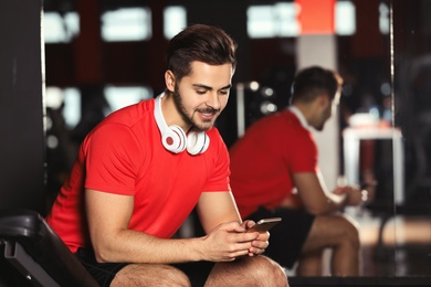 Young man with headphones and mobile device at gym