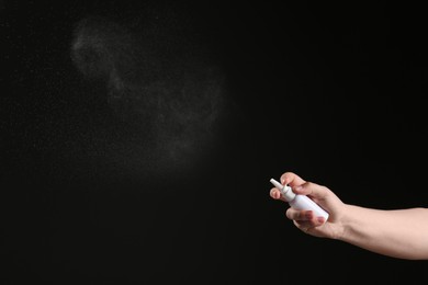 Nasal congestion. Woman spraying remedy from bottle on black background, closeup