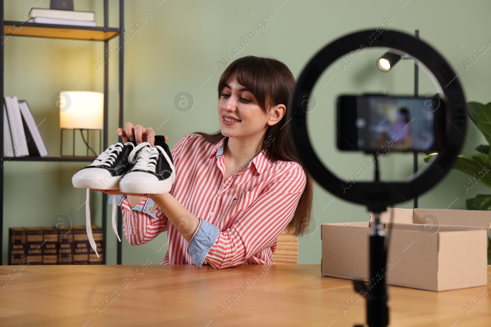 Photo of Smiling fashion blogger recording video while talking about sneakers at home