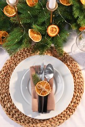 Photo of Festive place setting with beautiful dishware, fabric napkin and dried orange slice for Christmas dinner on white table, flat lay
