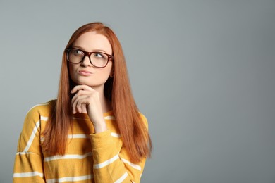 Portrait of thoughtful young woman with gorgeous red hair on grey background, space for text